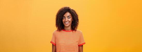 à la taille coup de étonné et excité charmant africain américain femme avec frisé coiffure éclater yeux de frisson et joie souriant largement étant surpris par génial cadeau plus de Orange Contexte photo