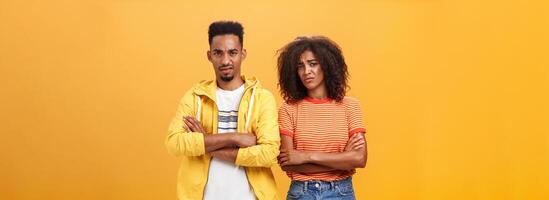 deux copains Ne pas aimer boiteux idée de copain. portrait de mécontent pas impressionné africain américain homme et femme traversée bras sur poitrine dans aversion renfrogné douteux et déçu plus de Orange mur photo