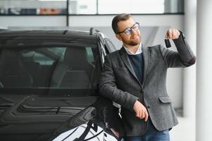 portrait de une Beau vendeur dans le costume permanent près le voiture dans le salle d'exposition photo