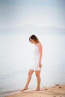 magnifique femme dans une blanc robe en marchant sur le plage.détendu femme respiration Frais aérien, émotionnel sensuel femme près le mer, profiter été.voyage et vacances. liberté et inspiration concept photo