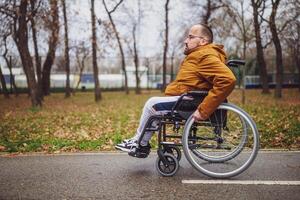 portrait de paraplégique handicapé homme dans fauteuil roulant dans parc. il est roulant sur sentier. photo