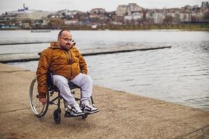content paraplégique handicapé homme dans fauteuil roulant par le lac. il est roulant sur passerelle. photo