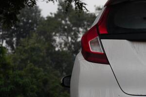 arrière côté de blanc voiture parking dans le nuit temps. sur corps de voiture avec laissez tomber de l'eau de pluie. Contexte de des arbres. photo