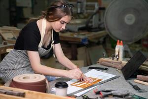 une Jeune femme est formation à être une Charpentier dans le atelier. elle travaux avec une portable ordinateur dans une bois atelier. femelle Charpentier contact les clients par téléphone intelligent. pme photo