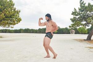 Jeune musclé homme exercice sur le plage, Jeune musclé homme Faire musculation des exercices sur le plage, athlétique Jeune homme sur le plage photo