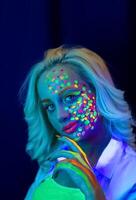 portrait de une femme avec peint affronter, femme avec uv maquillage dans studio, portrait de une femme dans carnaval masque, le femme est décoré dans une ultra-violet poudre photo