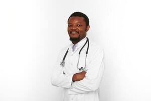 souriant noir barbu médecin homme franchi bras dans blanc peignoir avec stéthoscope, blanc Contexte photo