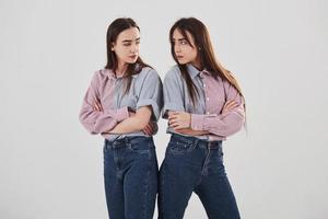 offensé et regarde les autres avec colère. deux soeurs jumelles debout et posant en studio avec fond blanc photo