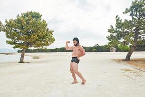 Jeune musclé homme exercice sur le plage, Jeune musclé homme Faire musculation des exercices sur le plage, athlétique Jeune homme sur le plage photo