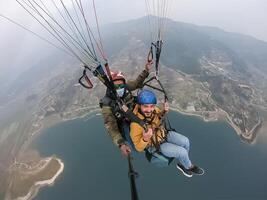 parapente dans le montagnes, le deux les personnes sur le Haut de le montagne, le parachutistes sont en volant avec une parachute photo