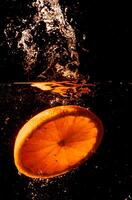 Orange dans l'eau sur une noir Contexte. Orange tranche dans le l'eau. photo