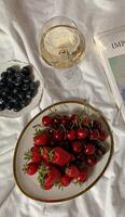 encore la vie avec une verre de blanc du vin et une assiette de des fraises et cerises photo