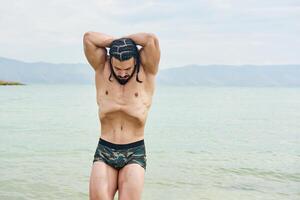 Jeune musclé homme exercice sur le plage, Jeune musclé homme Faire musculation des exercices sur le plage, athlétique Jeune homme sur le plage photo