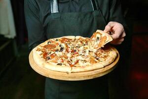 la personne en portant une Pizza sur une en bois plateau photo