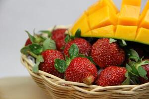 une panier de des fraises et mangues sur le Coupe planche sur blanc Contexte photo