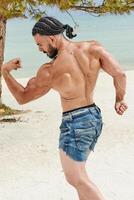 Jeune musclé homme exercice sur le plage, Jeune musclé homme Faire musculation des exercices sur le plage, athlétique Jeune homme sur le plage photo