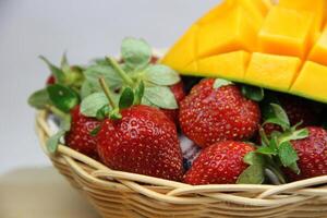 une panier de des fraises et mangues sur le Coupe planche sur blanc Contexte photo