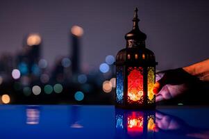lanterne en portant par main sur table avec nuit ciel et ville bokeh lumière Contexte pour le musulman le banquet de le saint mois de Ramadan Karim. photo