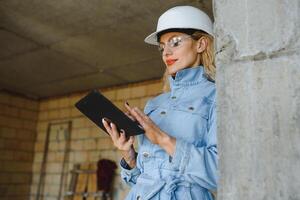 absorbé dans le travail de une femme ingénieur travail avec une tablette sur le Contexte de le construction placer. portrait de une Jeune architecte, protecteur équipement. sélectif se concentrer. photo