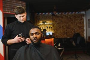 fermer de processus de garniture de cheveux dans coiffeur magasin. qualifié coiffeur en gardant tondeuse dans mains et corriger forme de cheveux à Masculin client séance sur chaise. concept de la Coupe de cheveux et rasage. photo