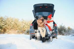 souriant couple avec chien séance dans ouvert suv voiture tronc dans neigeux forêt. profiter chaque autre dans actif hiver vacances. photo