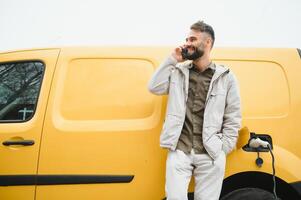 décontractée homme près électrique voiture attendre pour le terminer de le batterie mise en charge processus photo