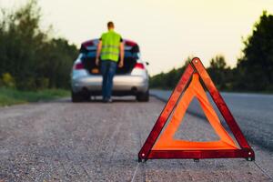 cassé argent luxe voiture urgence accident. homme chauffeur installation rouge Triangle Arrêtez signe sur route. sport voiture tourné sur clignotants technique problèmes sur le route. sécurité procédure lorsque ayant véhicule cassé vers le bas photo