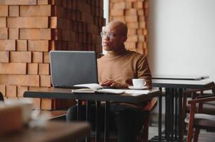 afro-américain entrepreneur portant chemise avec roulé en haut manches à la recherche par fenêtre avec réfléchi et sérieux visage expression, sentiment nerveux avant réunion avec affaires les partenaires à café. photo