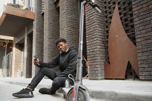 Jeune africain américain gars avec électrique scooter dans le ville. le concept de écologique transport. photo