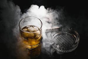 une verre de whisky ou Bourbon avec la glace cubes et une cigare sur une noir ardoise avec fumée photo