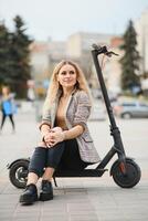 Jeune femme sur électro scooter dans ville. femme équitation scooter dans le coucher du soleil lumière dans rue photo