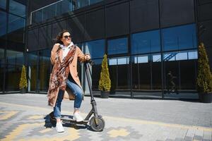 Jeune magnifique femme équitation un électrique scooter à travail, moderne fille, Nouveau génération, électrique transport, écologie, écologique transport, le coucher du soleil photo