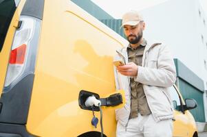 décontractée homme près électrique voiture attendre pour le terminer de le batterie mise en charge processus photo