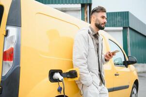 décontractée homme près électrique voiture attendre pour le terminer de le batterie mise en charge processus photo