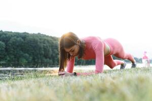 Jeune caucasien femme Faire actif formation exercice sur une yoga tapis près le rivière dans été. concept de en bonne santé mode de vie photo