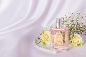 élégant bouteille de aux femmes parfum avec délicat floral fragrance sur blanc satin Contexte parmi thé des roses et perle perles. une copie espace. photo
