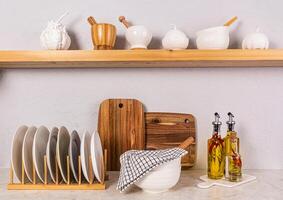 brillant cuisine espace dans une moderne cuisine. les serviettes, une ensemble assiette supporter de cuisine vaisselle. décoratif citrouilles sur un ouvert en bois étagère. de face voir. photo