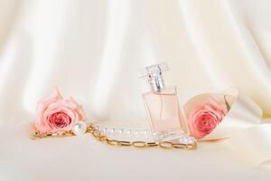 une magnifique composition avec un élégant parfum bouteille, rose des roses, une or Collier et une satin ruban. délicat satin beige Contexte. photo