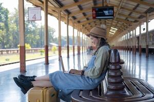 fille en utilisant une portable tandis que attendre dans une train gare, fille sur train station avec bagage travail sur portable ordinateur, portable dans utiliser, est assis avec une valise photo