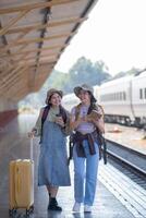 deux Jeune asiatique copains les filles avec sacs à dos à chemin de fer station attendre pour former, deux magnifique femmes en marchant le long de Plate-forme à train station photo