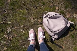 femelle jambes dans jeans et rose baskets sont permanent dans une sol de forêt avec sac à dos. photo