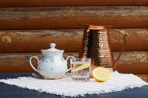 cuivre lanceur et l'eau avec citron sur le en bois table Extérieur. été encore la vie avec l'eau et lanceur. photo