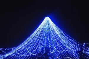 embrasé bleu dôme de une Noël arbre contre le nuit ciel. l'hiver. rue et de fête Nouveau années éclairage sur le ville rue. photo