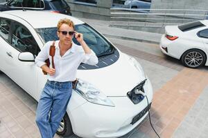 une Beau Jeune homme est mise en charge le sien moderne électrique auto. photo