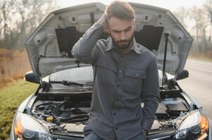 triste chauffeur en portant le sien tête ayant moteur problème permanent près cassé voiture sur le route. voiture panne concept photo