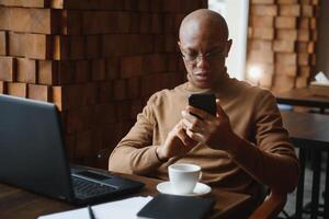 africain homme d'affaire parlant sur téléphone séance à café tableau, occupé entrepreneur travail lointain dans café maison avec portable papiers Parlant sur mobile, noir homme fabrication appel ayant le déjeuner dans cafétéria. photo