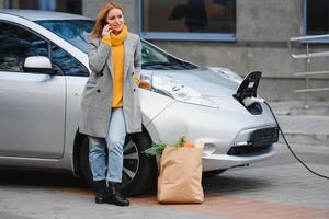 femme près une de location électrique auto. véhicule accusé à le mise en charge gare. photo