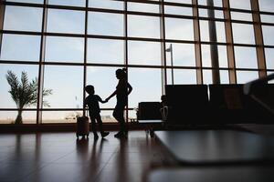 maman avec une peu fils et une valise à le aéroport. Voyage concept photo