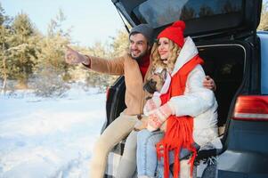 souriant couple avec chien séance dans ouvert suv voiture tronc dans neigeux forêt. profiter chaque autre dans actif hiver vacances. photo