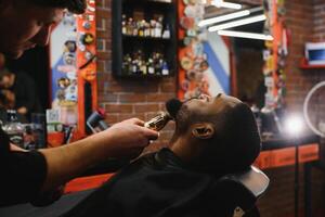 une coiffeur est Aller par le électrique Coupe et rasage machine pour le barbe de un Afro-américain brésilien garçon. photo